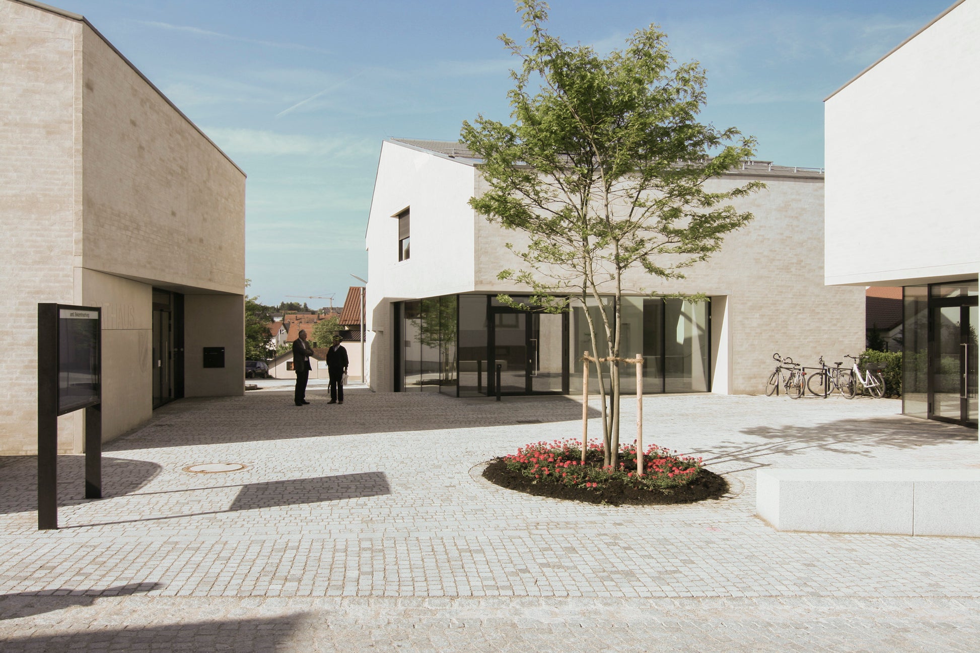 Freifläche der neuen Ortsmitte in Wettstetten mit zentralem Baum und umliegenden Gebäuden, darunter Rathaus und Saalgebäude.