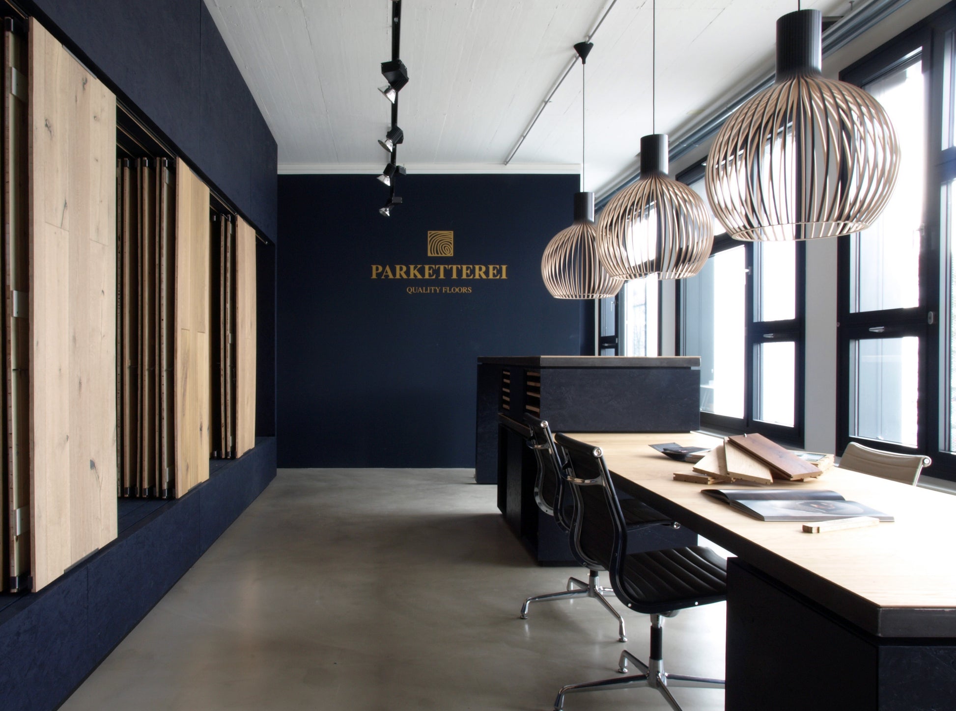 Langer Präsentationstisch mit Parkettmustern in einem Showroom, optimiert für die Zielgruppe Gewerbetreibende.