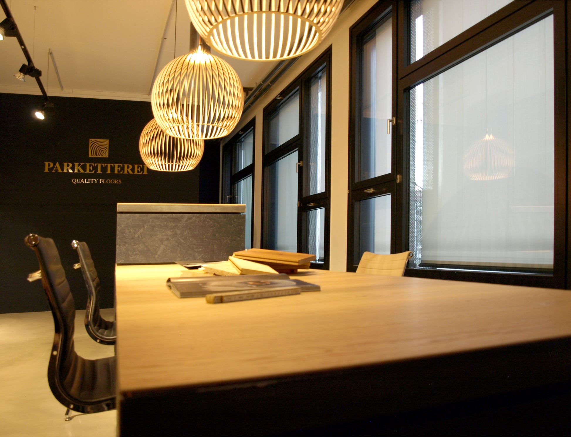 Detailaufnahme eines Arbeitsplatzes im Parkett-Showroom mit warmen Holztönen, eleganten Hängeleuchten und großzügigen Fenstern.