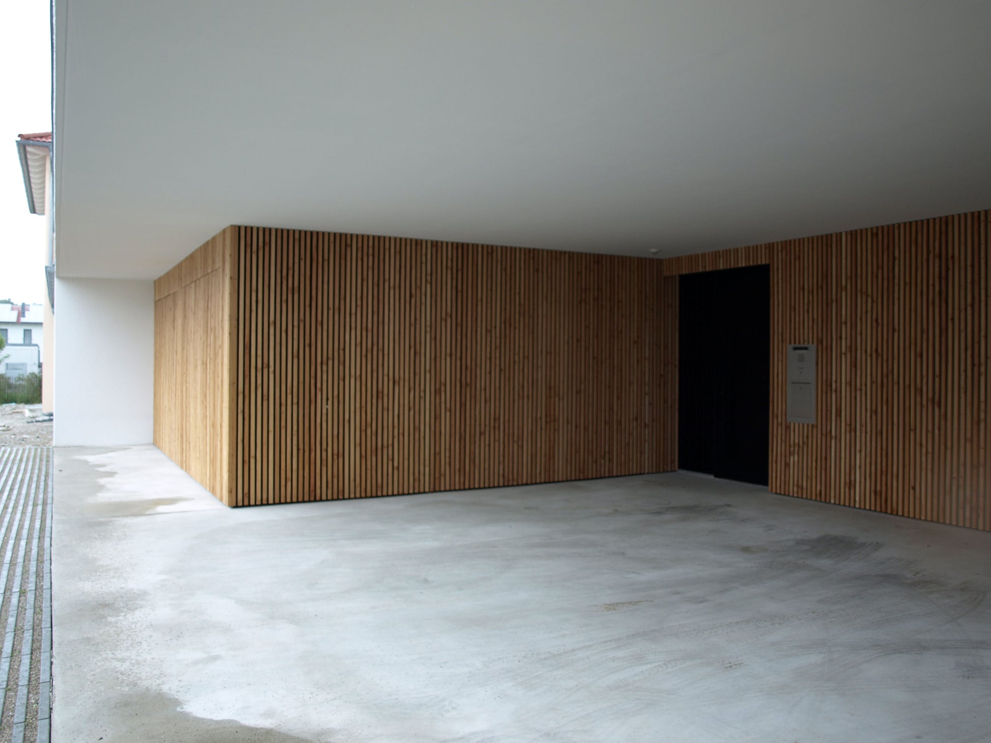 Überdachte Zufahrt mit Holzfassade und Betonboden, Teil eines modernen Einfamilienhauses mit nachhaltiger Bauweise.