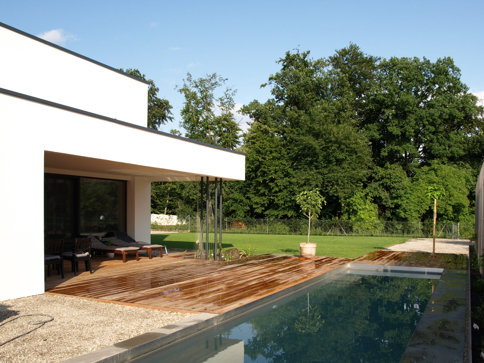 Außenansicht eines Einfamilienhauses mit Pool und Holzterrasse, eingebettet in eine grüne Gartenlandschaft.
